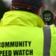 Person in a high-vis jacket reading "Community Speed Watch" using a radar speed gun outdoors.