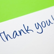 A pen writes "Thank you!" in blue ink on white paper with a green background.